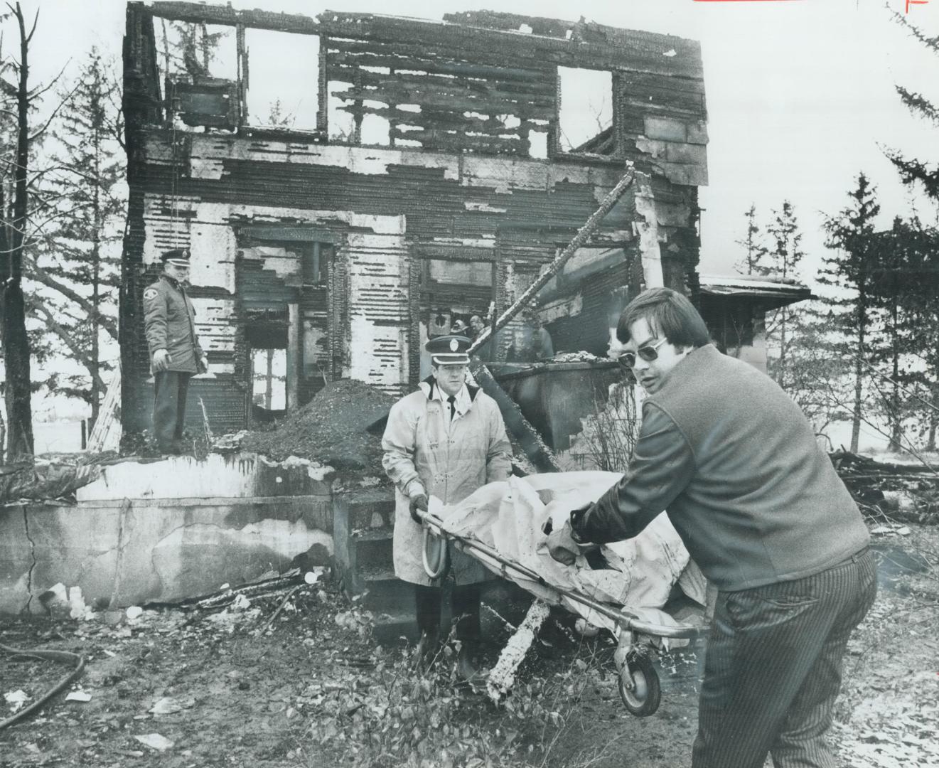 Two bodies are removed from a farmhouse near Brampton by Chinguacousy Township firemen after a fire took the lives of five of the six children of Raym(...)