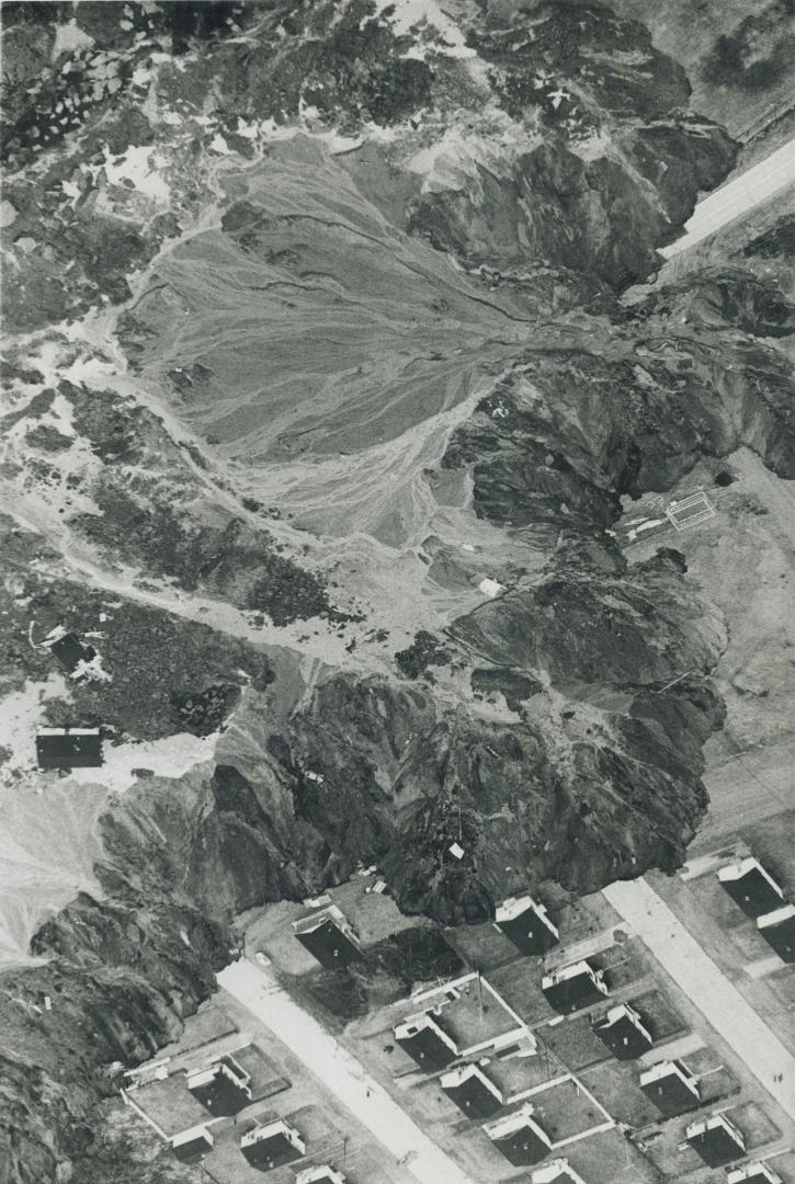 Neat frame houses cling to the edge of 100-feet-deep crater gouged in St