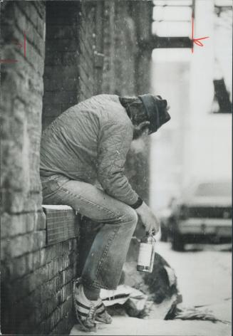 A derelict nurses a bottle in a downtown alley