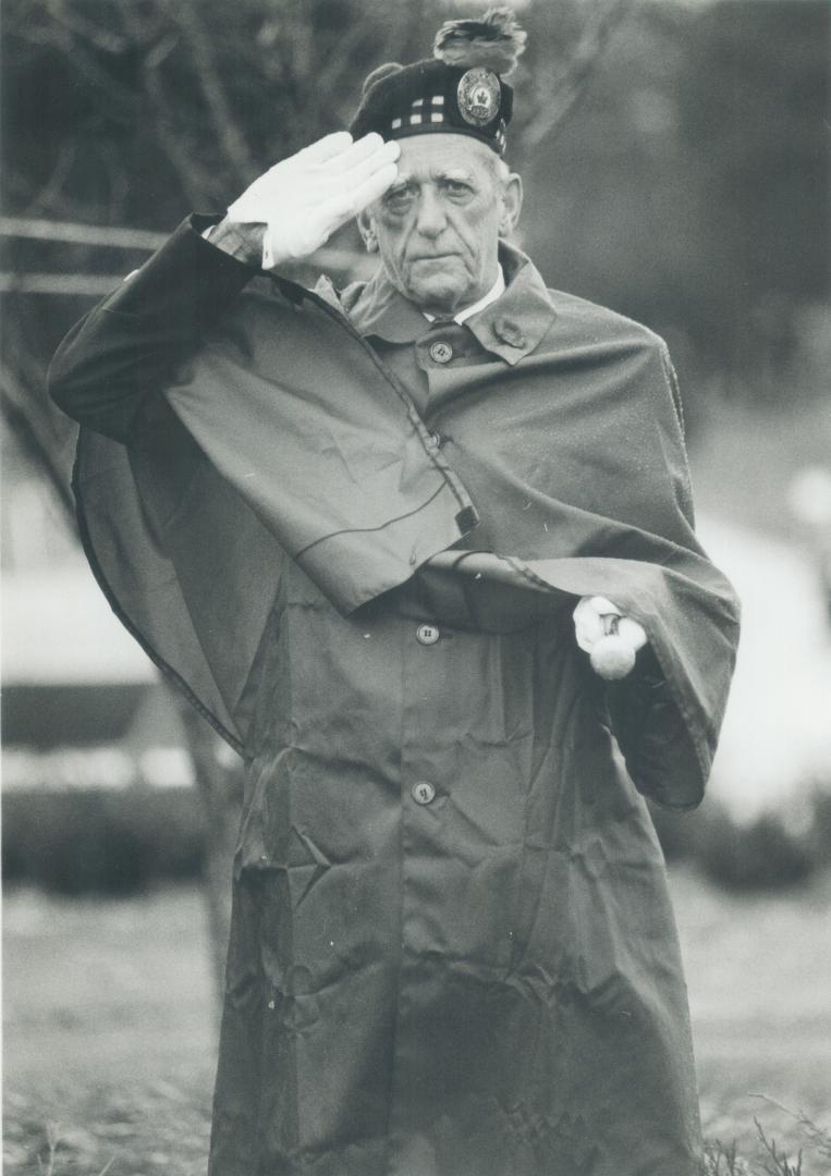 An older man in a uniform and long coat, wearing white gloves and a beret or tam, salutes while…