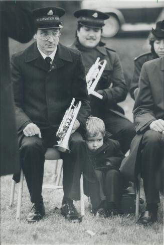 Barrington Venables, 4, huddles against his dad, Robert Venables, left, as a Salvation Army band waits to perform at an early Remembrance Day ceremony(...)