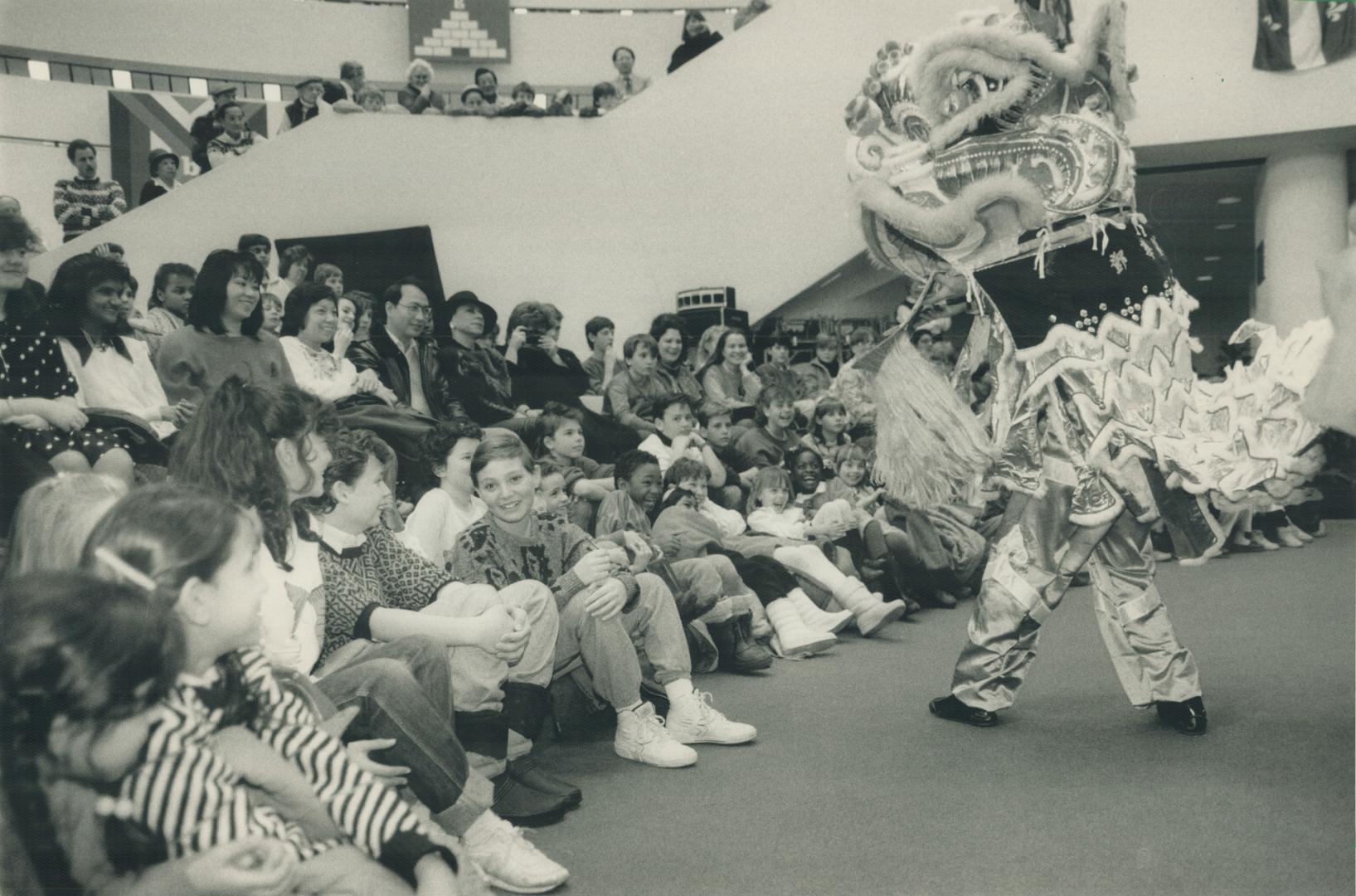 A dancer wearing a large, stylized Chinese Dragon head costume performs for a group of children…