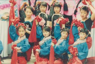 Girls in traditional matching vibrant clothing posing together with one arms raised holding red…