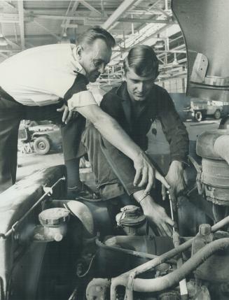 An airman Chief Warrant Officer Harry Kilbourn, gives orders to a soldier, Private William Fraser, working on a truck at Camp Borden