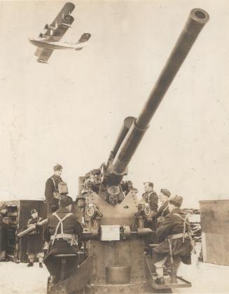 Lower left, one of the 3.7 ack-acks manned by its crew, while a giant Stranraer coastal patrol plane soars overhead