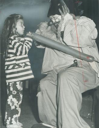 A Jolly Jesuit, Rev, John Naus, covers up his ears just before a balloon being blown up by Sandra Dowlings, 5, explodes