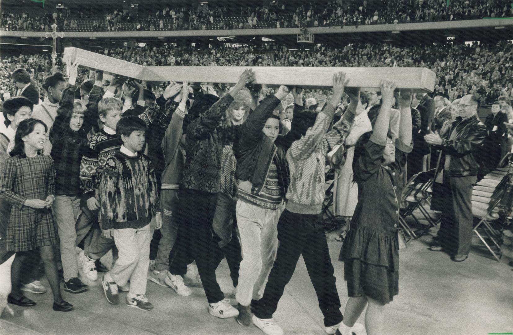 Keeping the faith: Anglican celebrants carry a giant cross through the SkyDome yesterday across the stadium floor that was stripped of its artificial turf