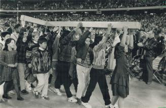 Keeping the faith: Anglican celebrants carry a giant cross through the SkyDome yesterday across the stadium floor that was stripped of its artificial turf