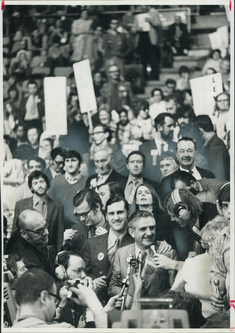 At moment of victory, newly elected New Democratic Party Leader David Lewis, surrounded by a sea of supporters, speaks into microphones while his son,(...)