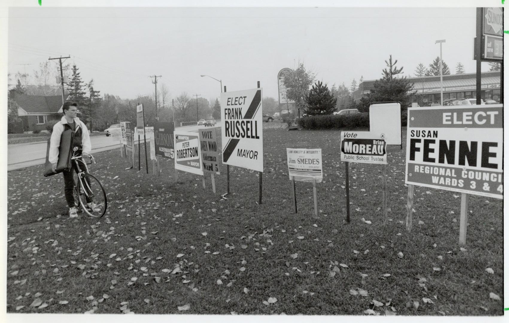 Signs of that time. Daniel Gareau, a student cycling to classes at Sheridan College's Brampton campus, takes time out to admire democracy in action in(...)