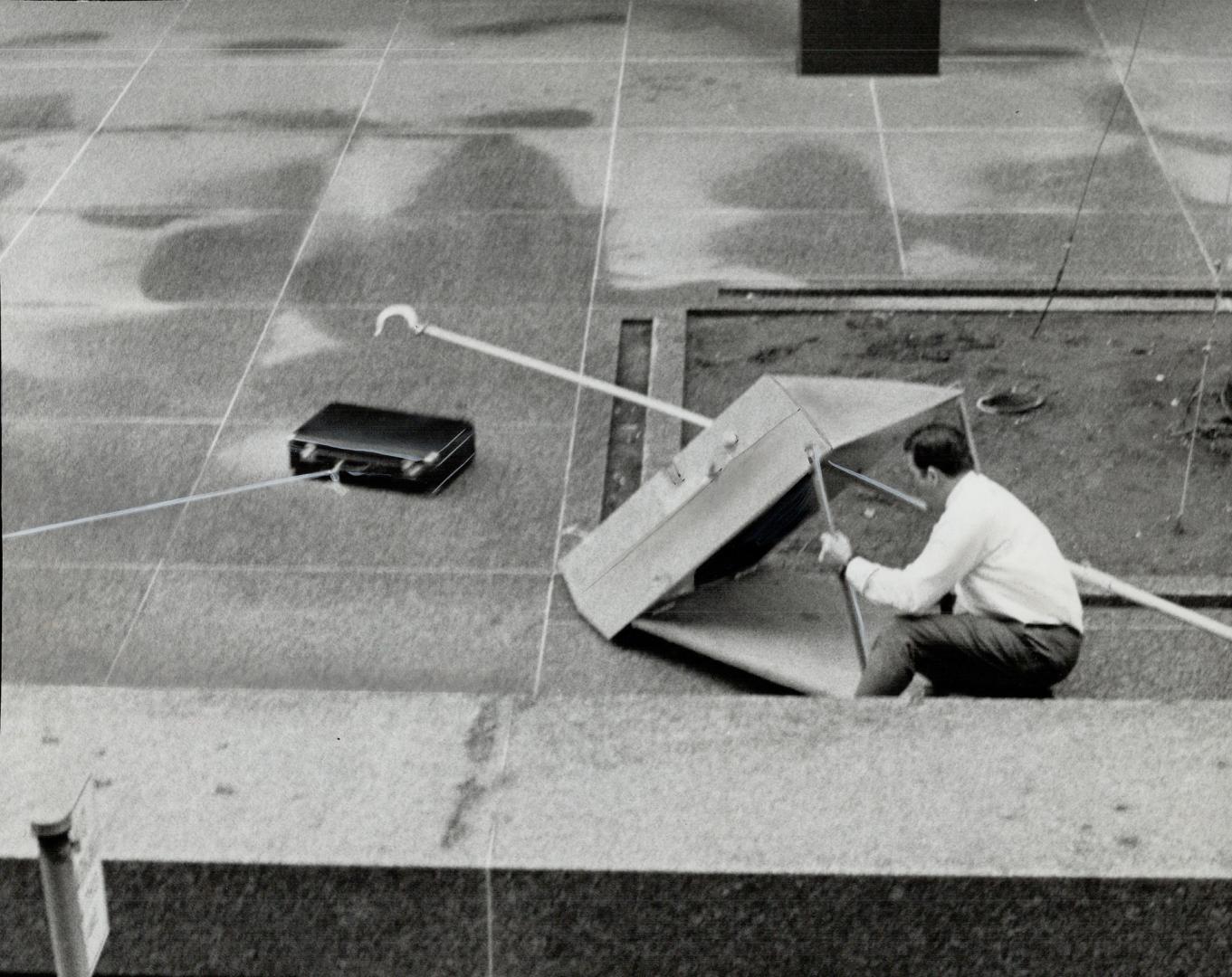 Groping gingerly forward with a grappling book as he crouches behind a heavy shield, Metro detective hooks the handle of a suspicious black suitcase f(...)