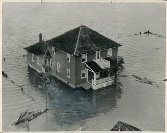 Their night of horror over, this Holland Marsh couple wave to a circling plane from the veranda of their water-logged home. [Incomplete]