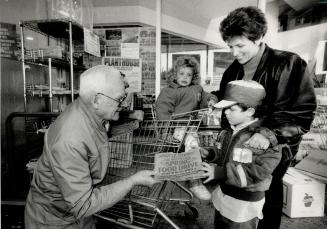 Grocery shoppers help the hungry, Food drive volunteer Sam Gilmore out a paper bag to Audrey Guth of North York before she does her grocery shopping with children Billy and Shauna