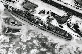 A Navy destroyer docked alongside a road, surrounded by floes of ice.