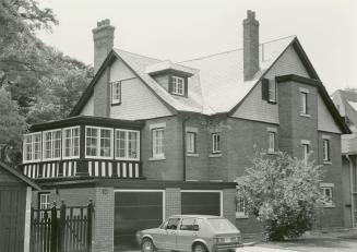 Image shows a three storey residential house with garages on the left. There is a car parked in…