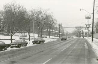 Image shows a street view with some cars parked on the left.