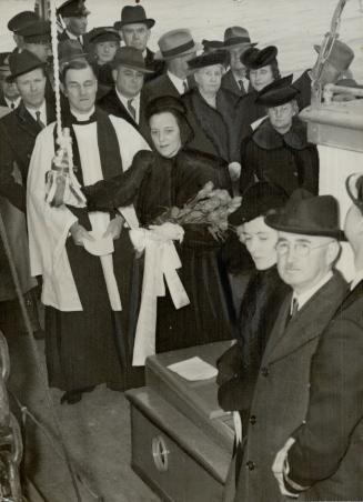 God Speed and Fair Sailing. Mrs. F. M. Deans, wife of the mayor, breaks a bottle of champagne over the bow of the corvette. Rev. Canon D. Russell Smith, also shown, formally dedicated the vessel