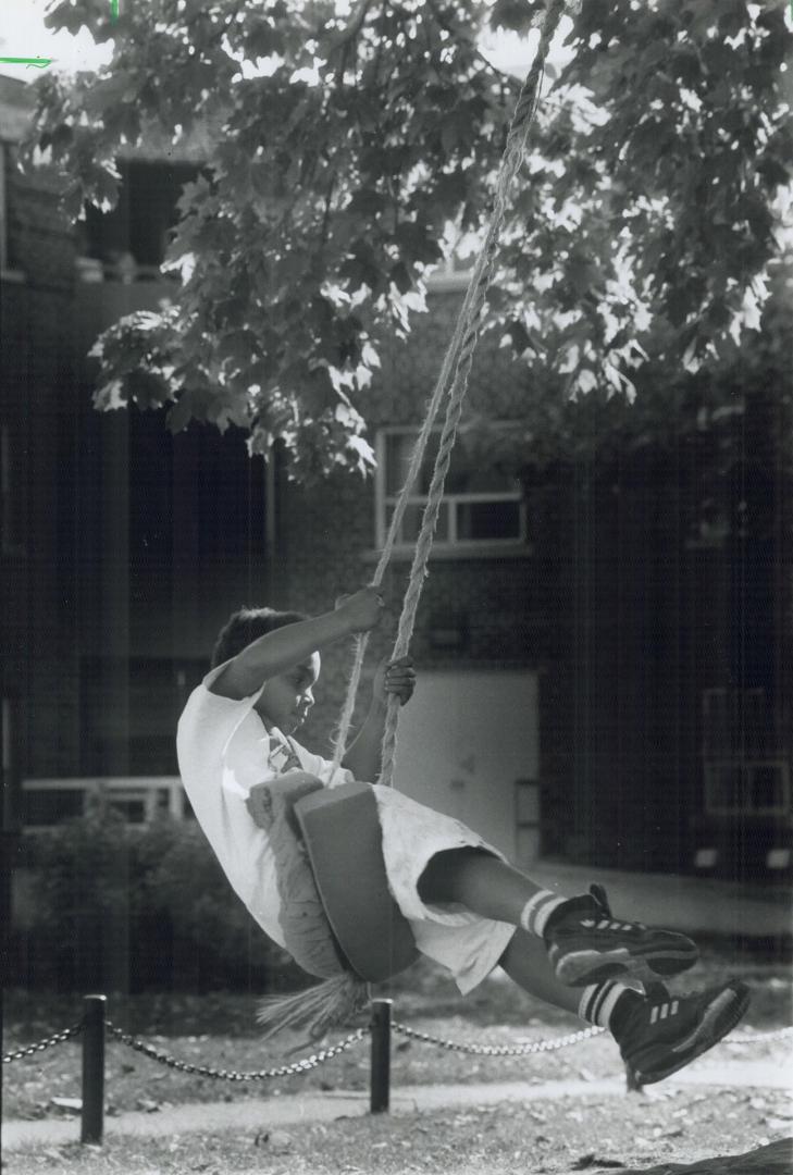 Swinging in the sun, Nowell Gordon, 9, spends part of his lunch break in the swing in front of his Gerrard St