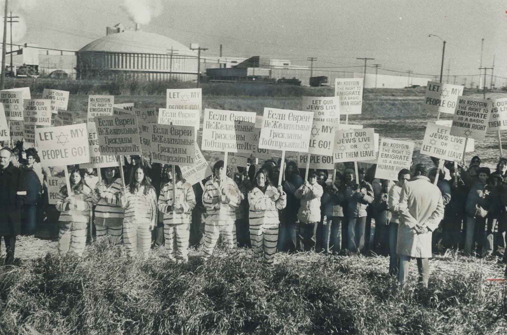 Costumed demonstrators wearing simulated prison uniforms stand in forefront of placard-carrying group waiting outside nuclear power station in Pickeri(...)