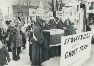 A coffin symbolizing the death of Stouffville was carried by boys and girls in monks' robes yesterday in a protest march on town hall to express fears(...)