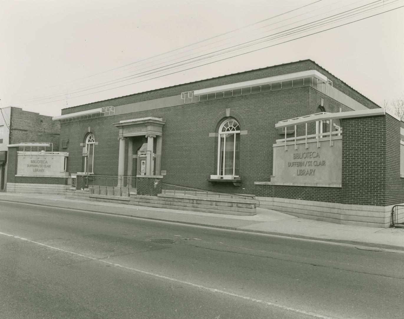 Street view of library with cement ramp at entrance. Etched signs on either side of entrance re…