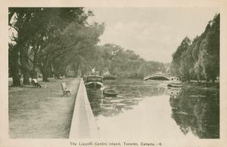 Black and white picture of a lagoon with boats and bridge and a park bench looking over the lag…