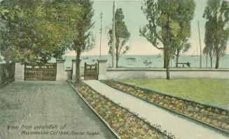 Picture of flower lined sidewalk leading to a lake with trees and lawn. 