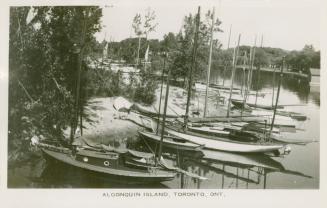 Black and white photograph and many sailboats without their sails docked at a beach.