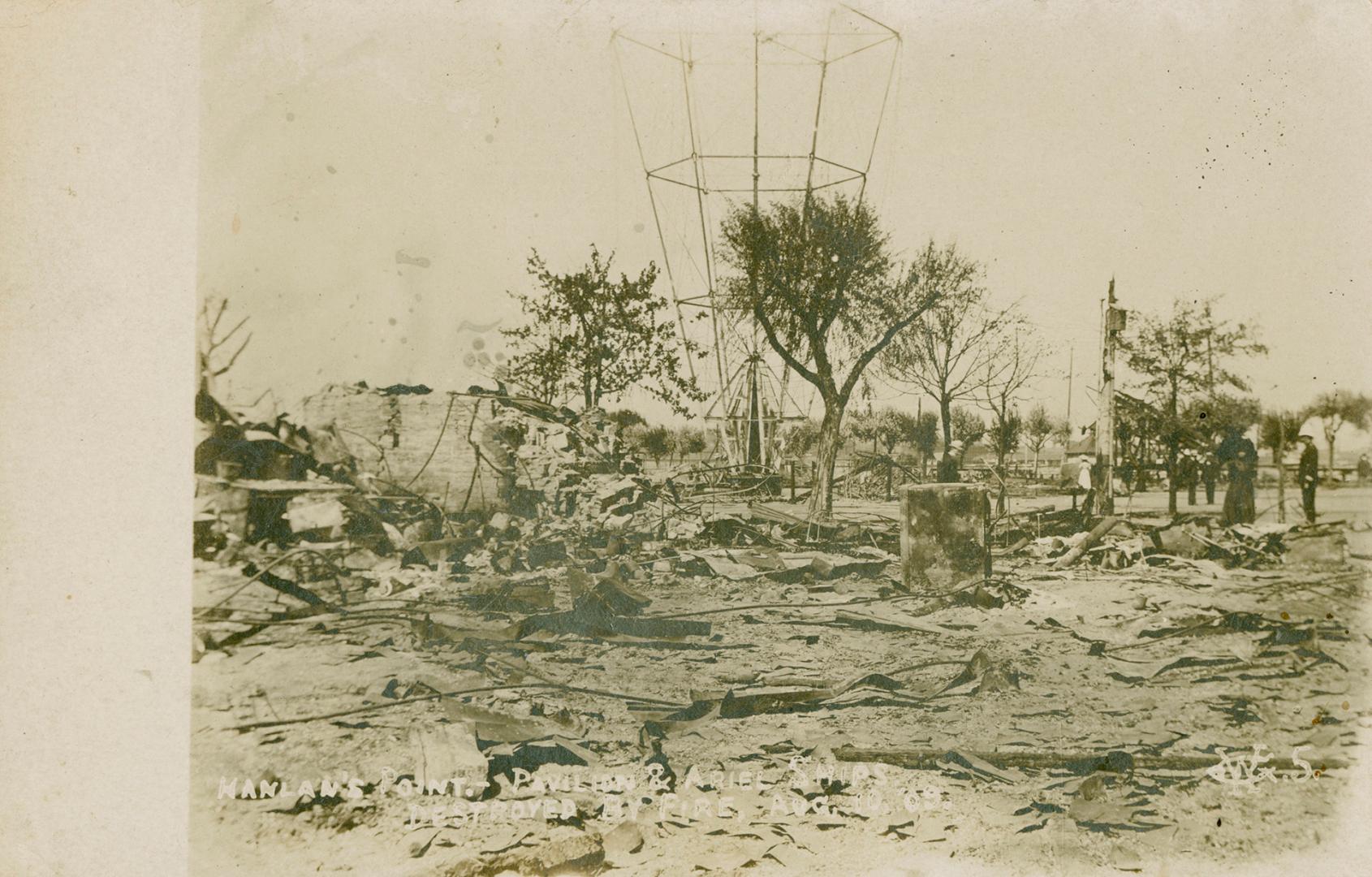 Black and white shows people examining the remains of a building destroyed by fire.