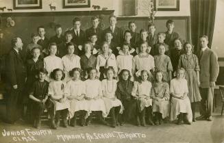 Picture shows a group of children posing for a picture with their two teachers in a classroom.