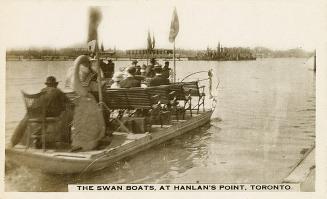 Black and white photo postcard of a Swan Boat ferry with people sitting aboard in rows of bench…