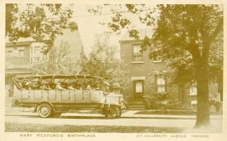 A group of people on a bus tour outside of the house where Mary Pickford was born.