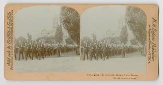 A parade of soldiers on a road in front of a huge building.