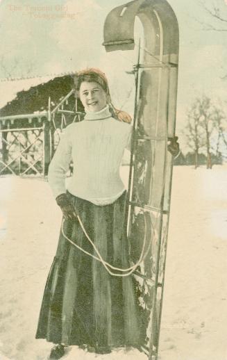 Girls standing in snow holding a toboggan.