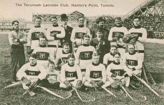 Black and white photo postcard of the Tecumseh Lacrosse Club, showing 19 members sitting in a g…