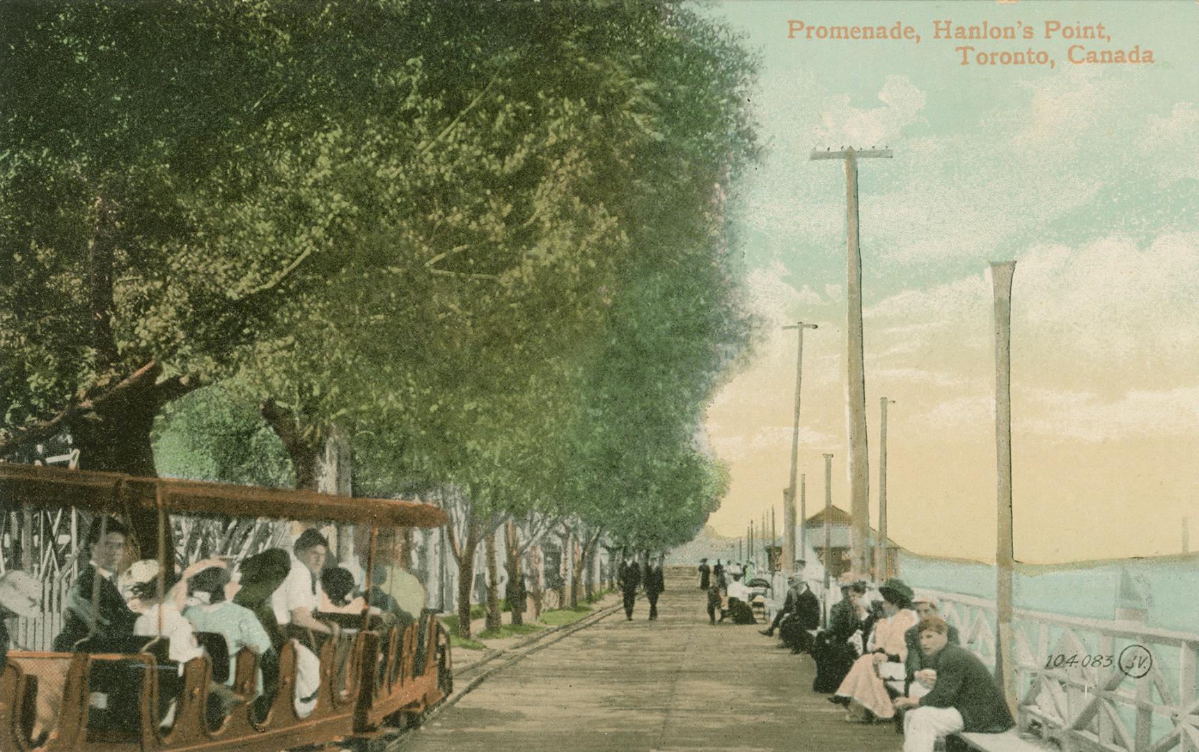 Colour photo postcard of the boardwalk at Hanlan's Point, with people siding on benches at the …