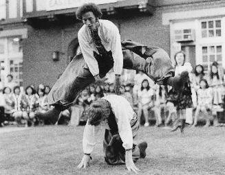 Male dancer jumping over the back of another dancer