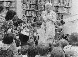 Woman demonstrating spinning wool on a spinning wheel for a group of children 