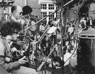 Three male musicians playing instruments at an outdoor concert 