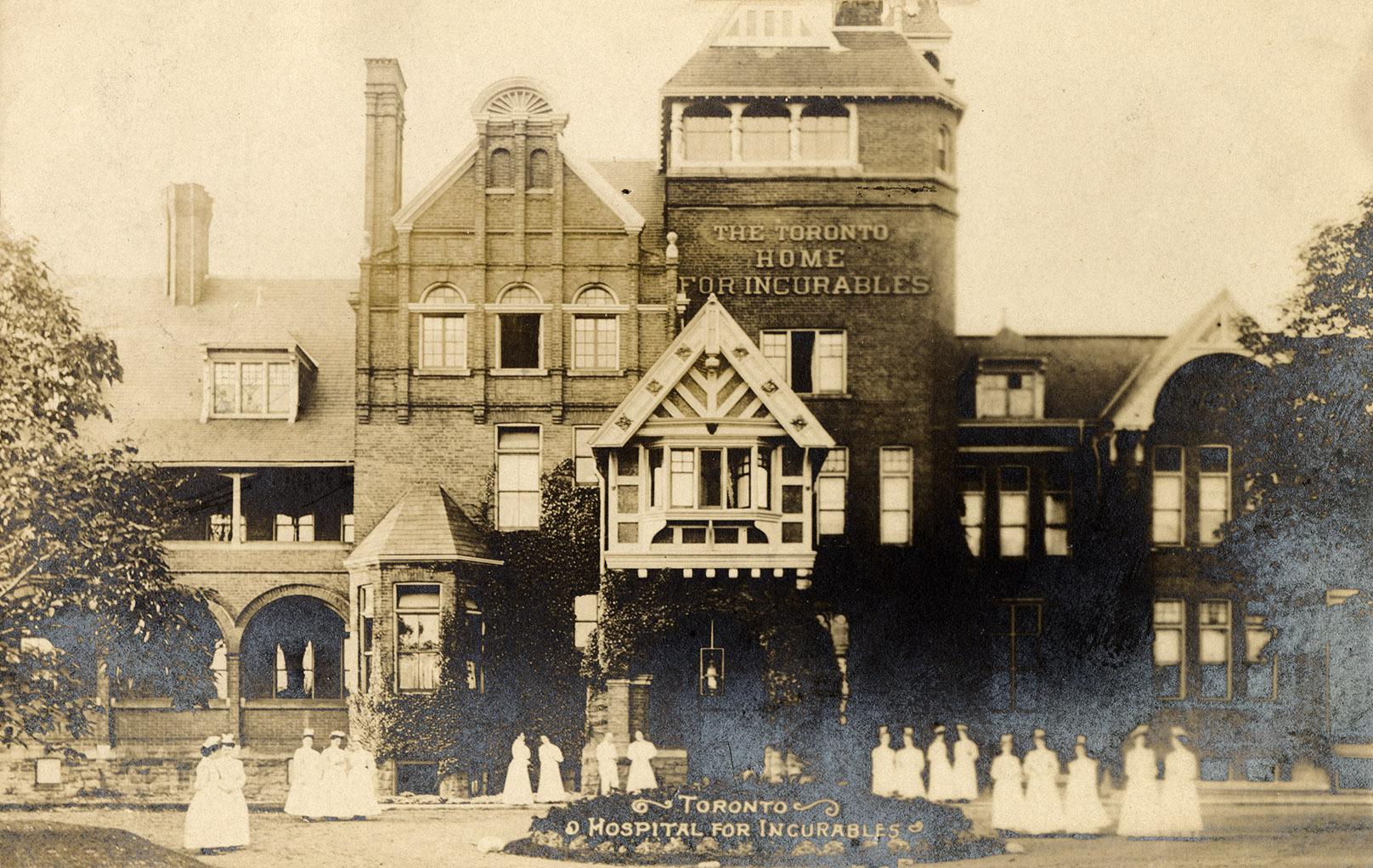 Black and white phonograph of a large, Victorian hospital with a large group of nurses in front…