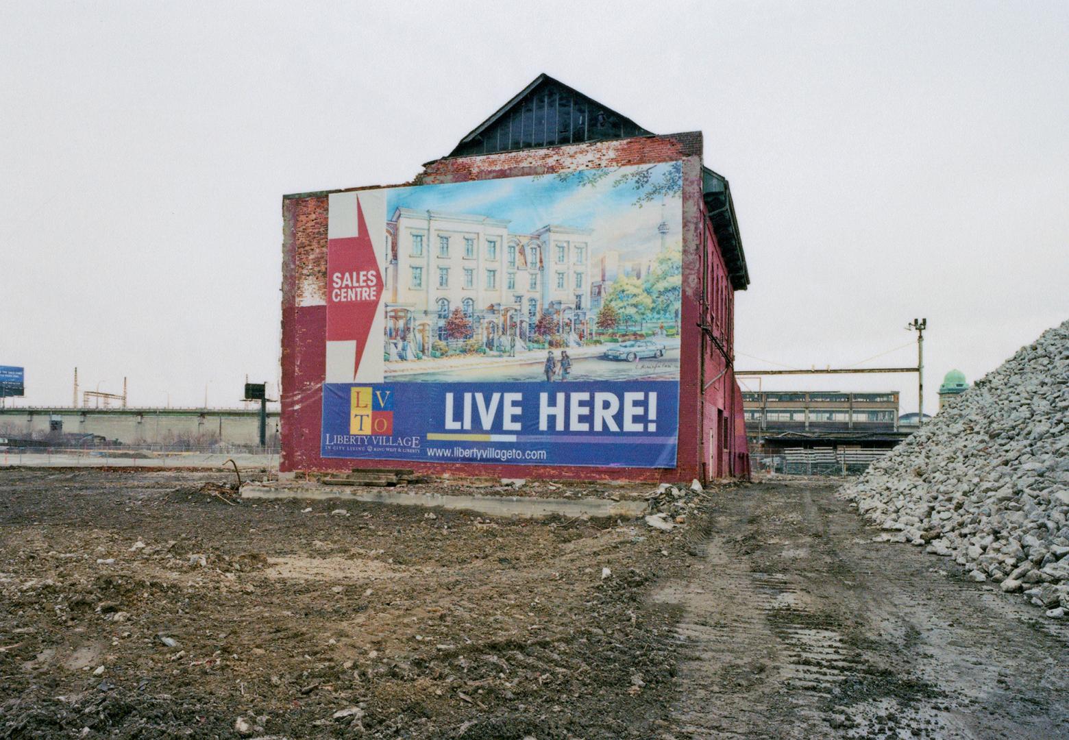 A photograph of a building in an otherwise empty lot, with construction rubble visible to the r…