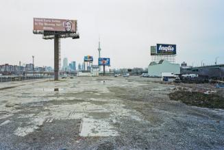 A photograph of a muddy parking lot. A building to the left has an Inglis billboard above it. T…