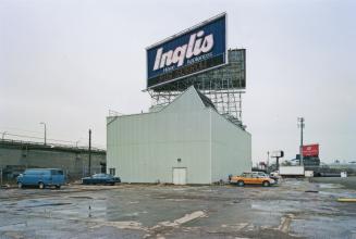 A photograph of a building surrounded by a parking lot, with an Inglis billboard above it.