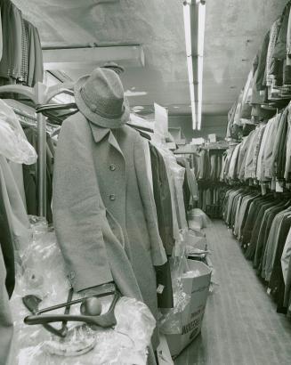 A photograph of a clothing store, with a coat, hat and apple in the foreground and racks of clo…