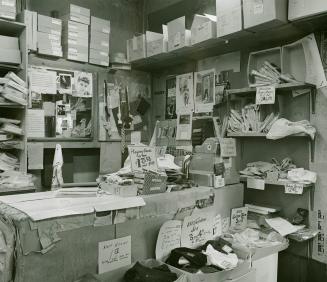 A photograph of a cash register on a sales counter, with boxes of playing cards and clothing vi…