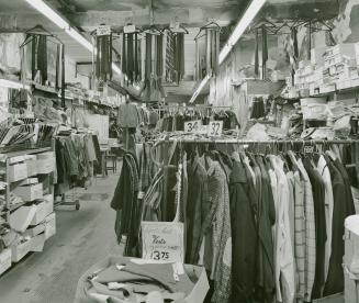 A photograph of a clothing shop, with racks of vests, coats, ties and other articles of clothin…