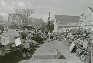 A photograph of a yard, with piles of old machinery, other metal objects, a crane, and resident…