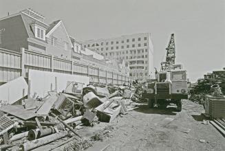 A photograph of a yard with piles of various metal objects and a crane, with residential houses…