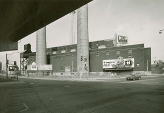 A photograph of an industrial facility with two smokestacks and a parking lot in the foreground…