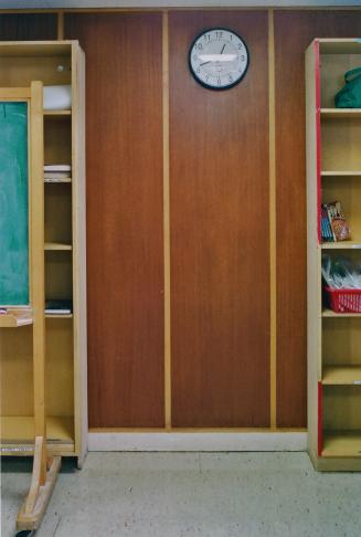 A photograph of a wall, with bookshelves and a clock.